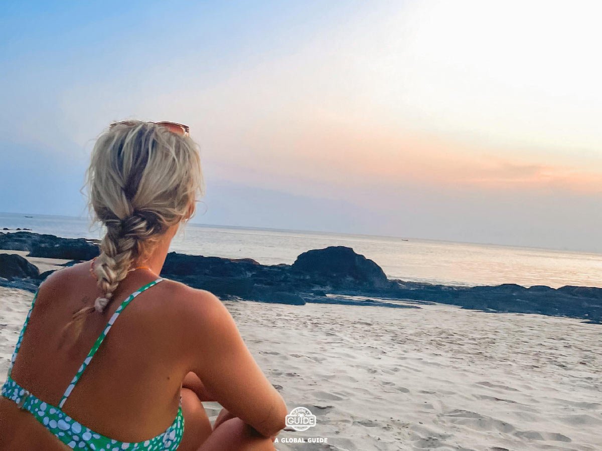 Girl sitting on beach watching sunset.