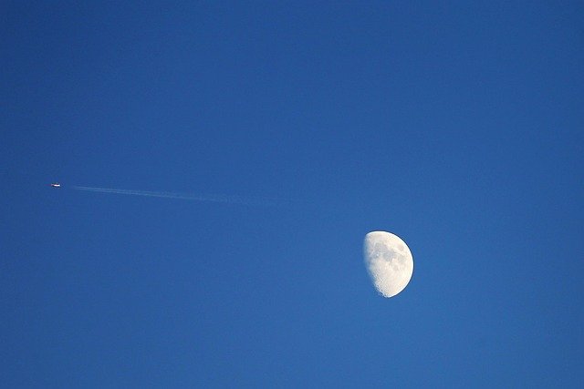 A airplane high in the sky next to the moon.