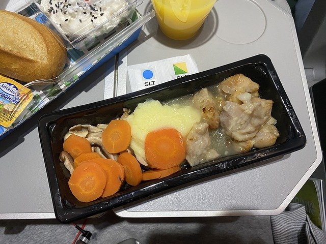 Airplane food in a container with the rest of the meal up in the corner.